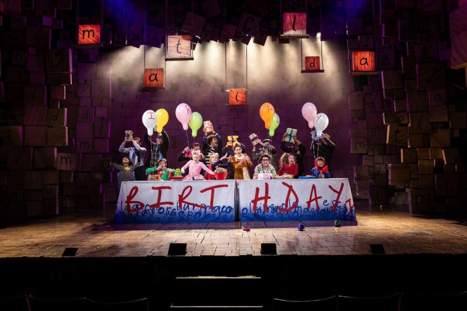 Matilda cast gathered around a birthday table on stage