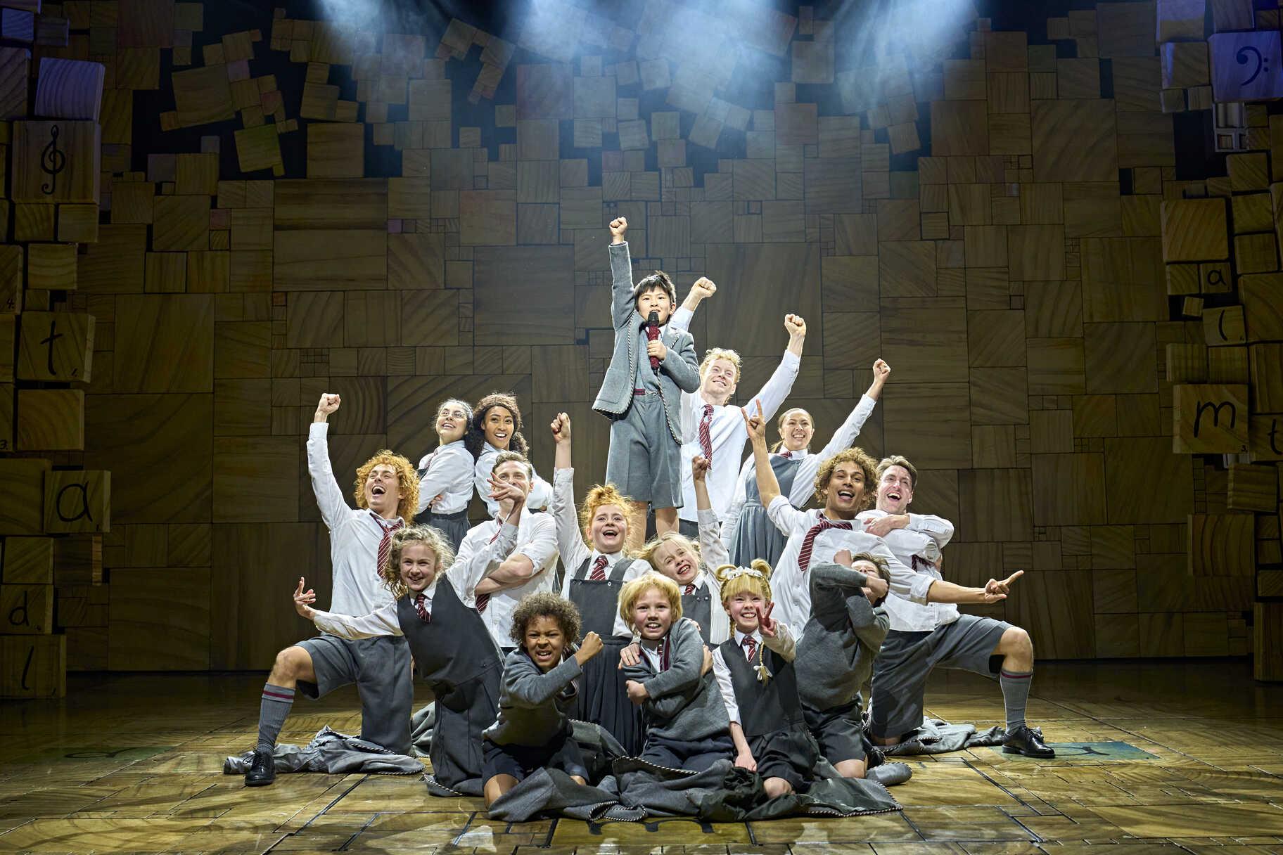 Matilda cast posing together on stage beneath letter blocks