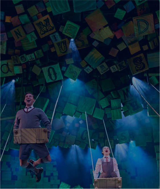 Adult performer and Matilda suspended above the stage among letter blocks