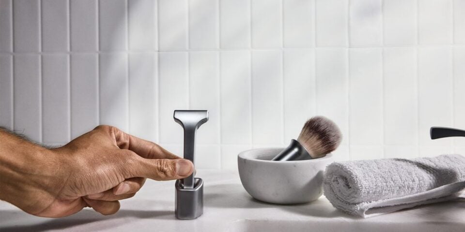 A hand lifting the Supply Single Edge SE razor from its stand
